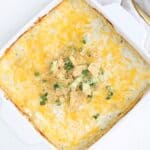 A layered enchilada bake topped in a square white baking dish.