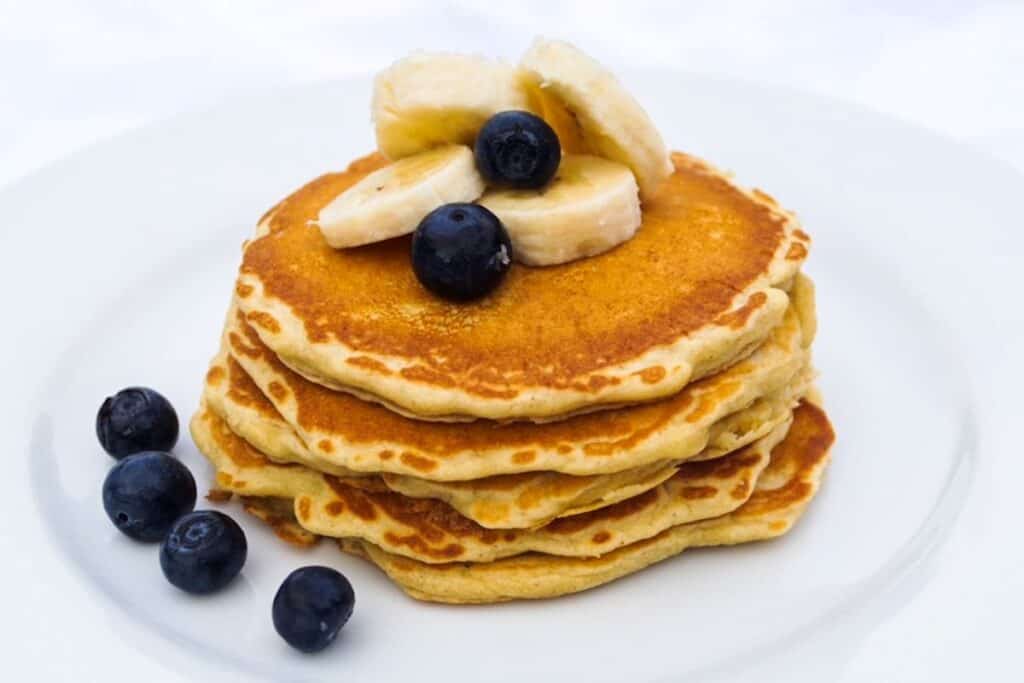 Stack of pancakes on a white plate topped with blueberries and banana slices.