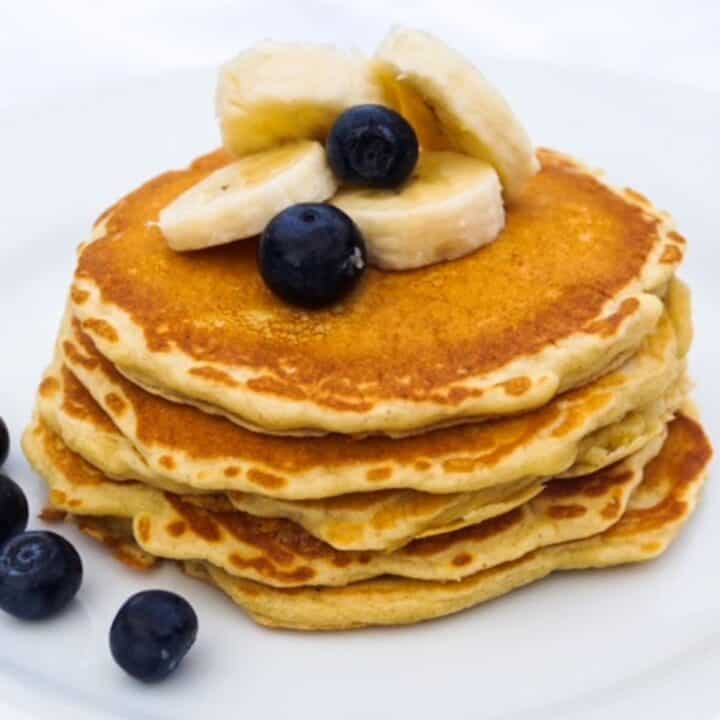 Stack of whole grain pancakes on a white plate topped with blueberries and banana slices.