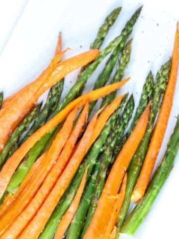 Top view of roasted carrots and asparagus on a white serving platter.