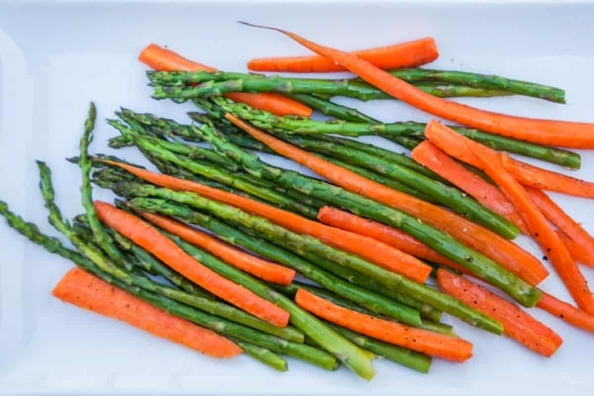 Roasted asparagus and thinly sliced carrots served on a white plate.