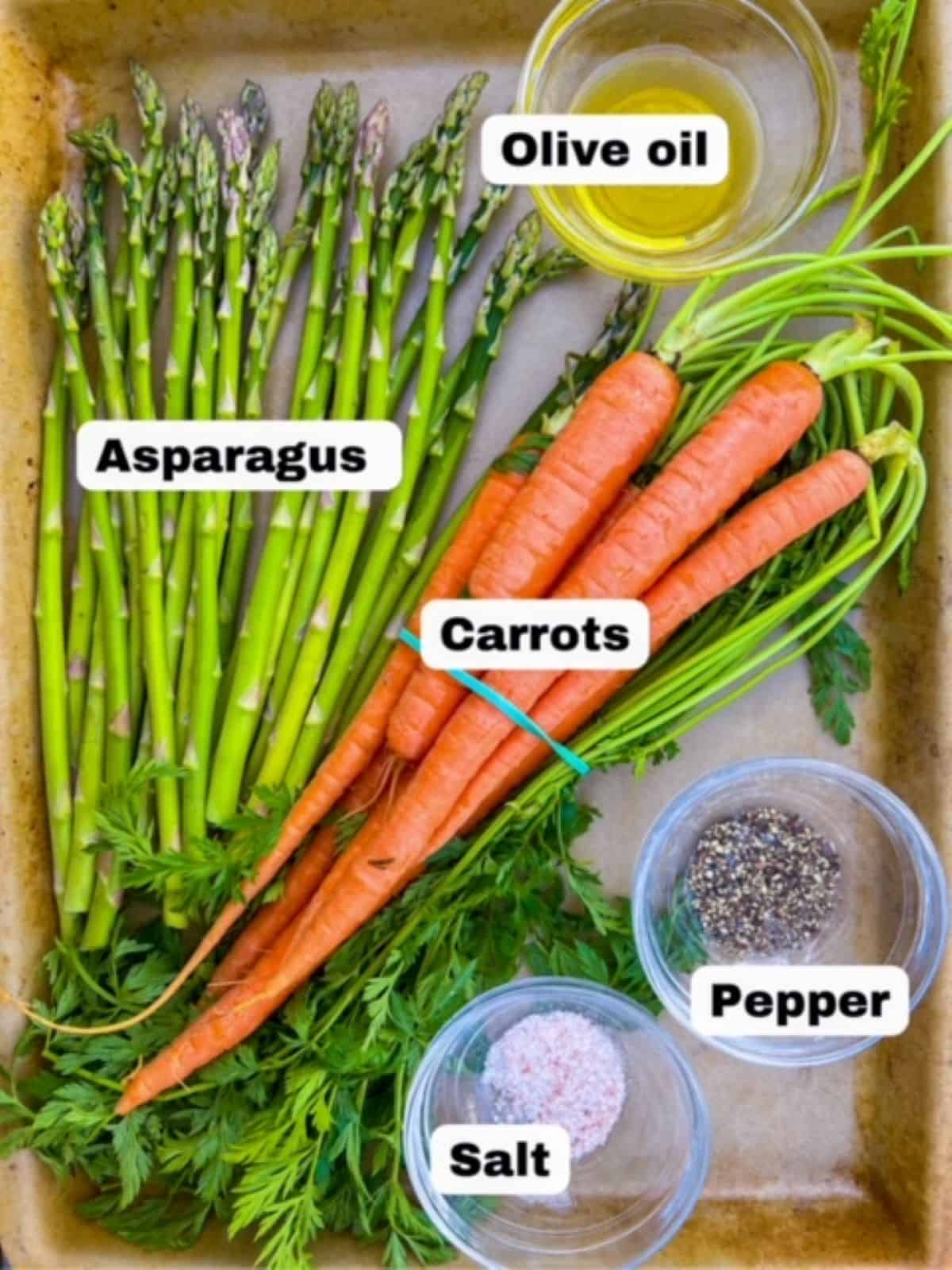 Asparagus, one bunch of carrots with stems, salt, pepper, and olive oil displayed on a baking stone.