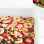 Banana baked oatmeal with strawberries and chocolate chips in a white baking dish.