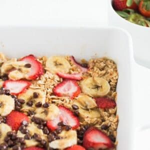 Banana baked oatmeal with strawberries and chocolate chips in a white baking dish.