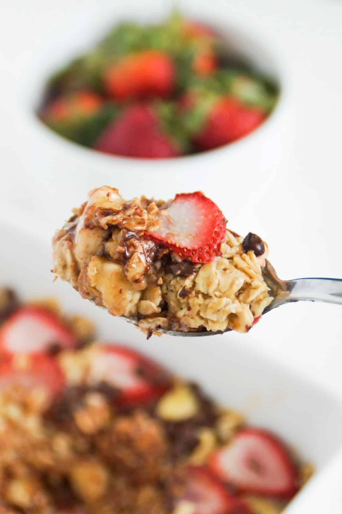 Banana and strawberry baked oatmeal on a spoon up close, with the rest in a serving dish in the background.