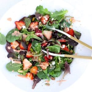 Strawberry Goat Cheese Salad in a large white serving bowl with tongs.