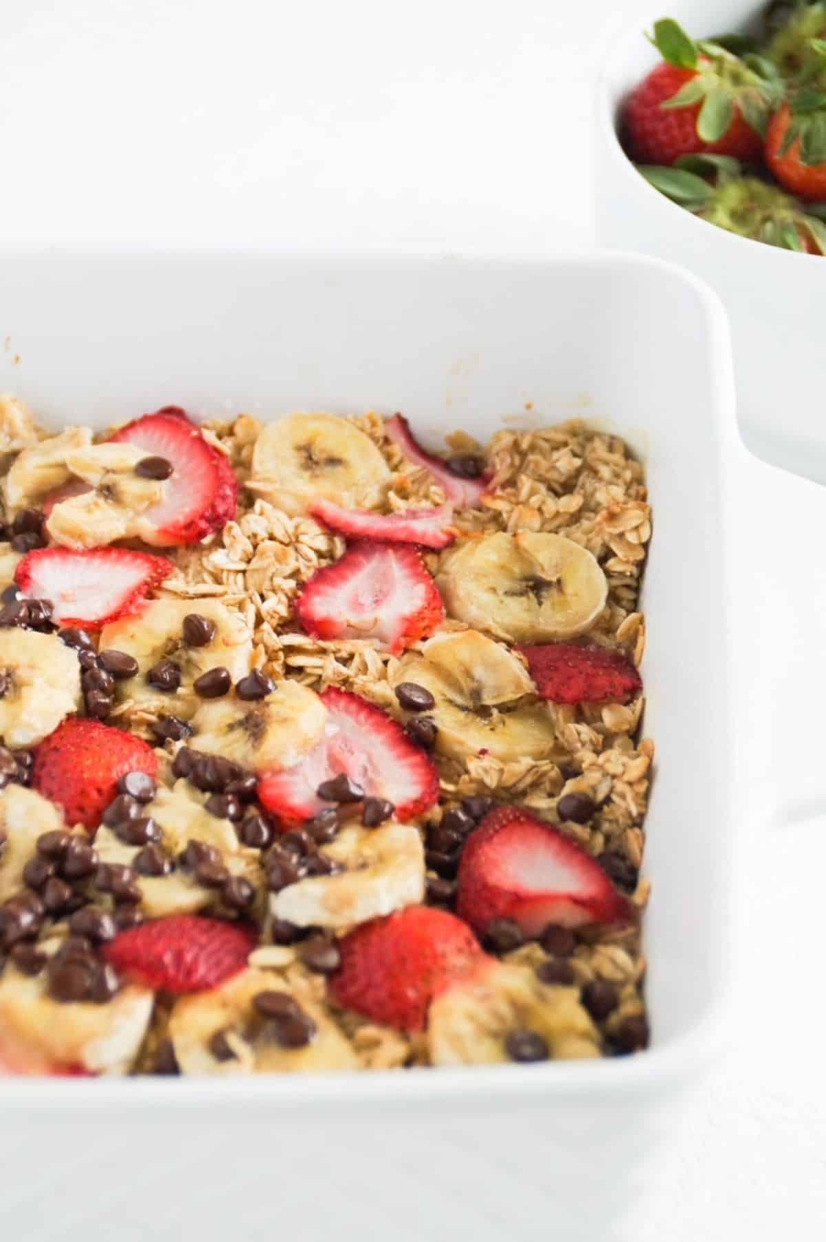 Banana baked oatmeal with strawberries and chocolate chips in a white dish.