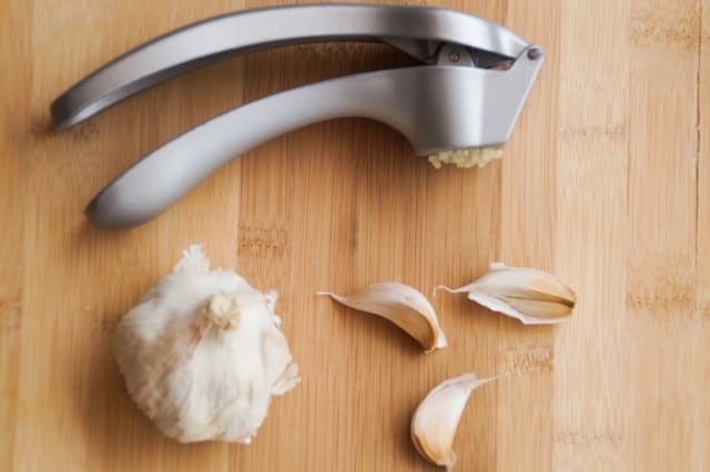 Garlic press with a bulb of garlic and garlic cloves