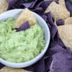 A bowl of guacamole surrounded by blue and white corn tortilla chips.
