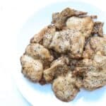 A pile of cooked marinated lemon pepper chicken on a white plate.