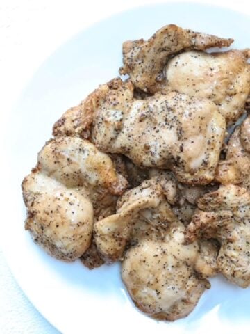 A pile of cooked marinated lemon pepper chicken on a white plate.