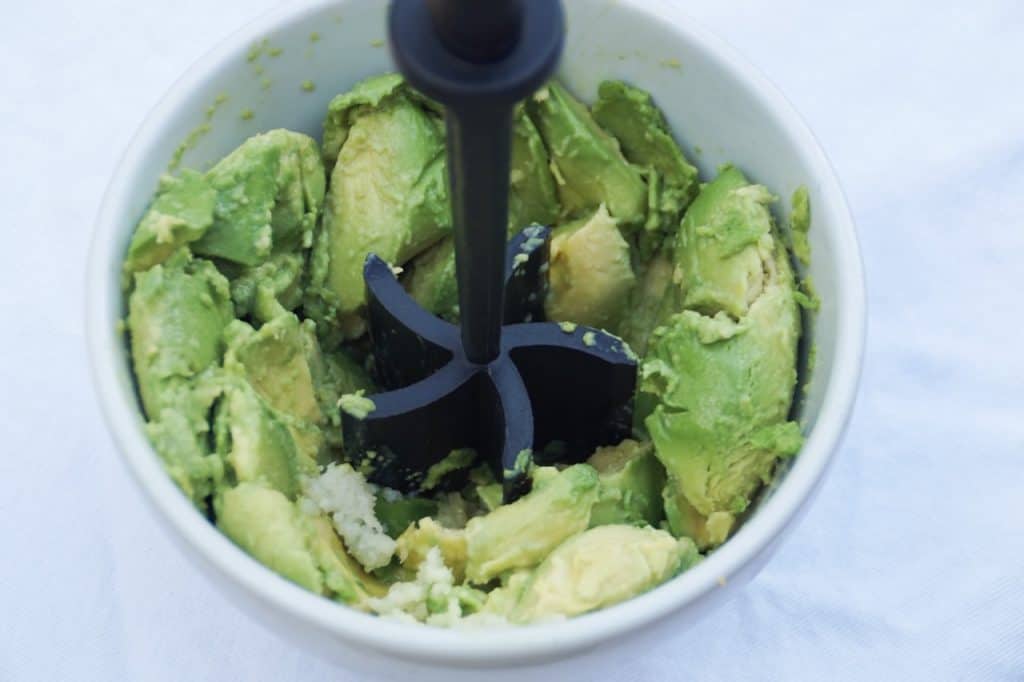 White bowl with avocados and a masher