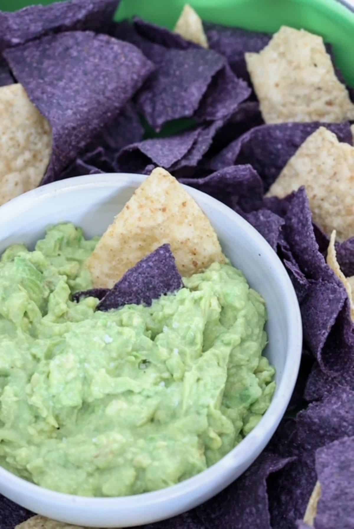 A bowl of guacamole surrounded by blue and white corn tortilla chips.
