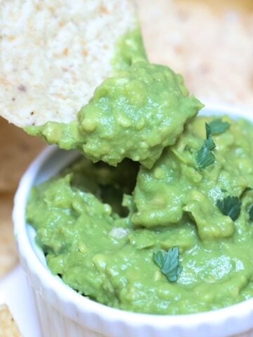 A chip being dipped into guacamole served in a white ramekin.