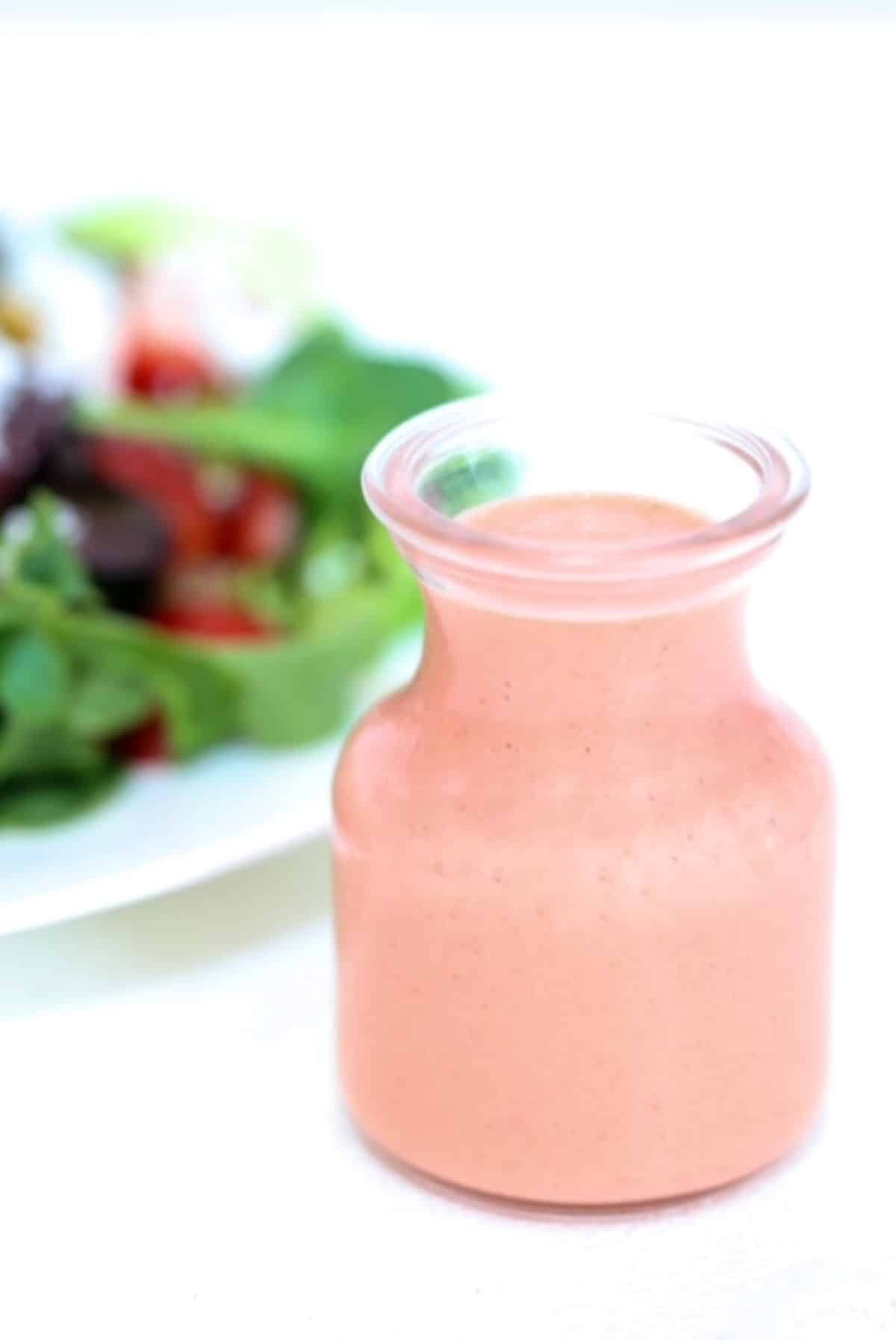Strawberry Balsamic Salad Dressing in a glass dressing jar with a salad in the background.