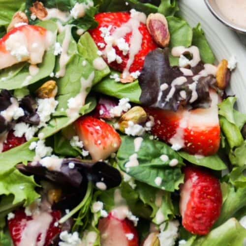 Strawberry goat cheese salad topped with dressing on a white plate.