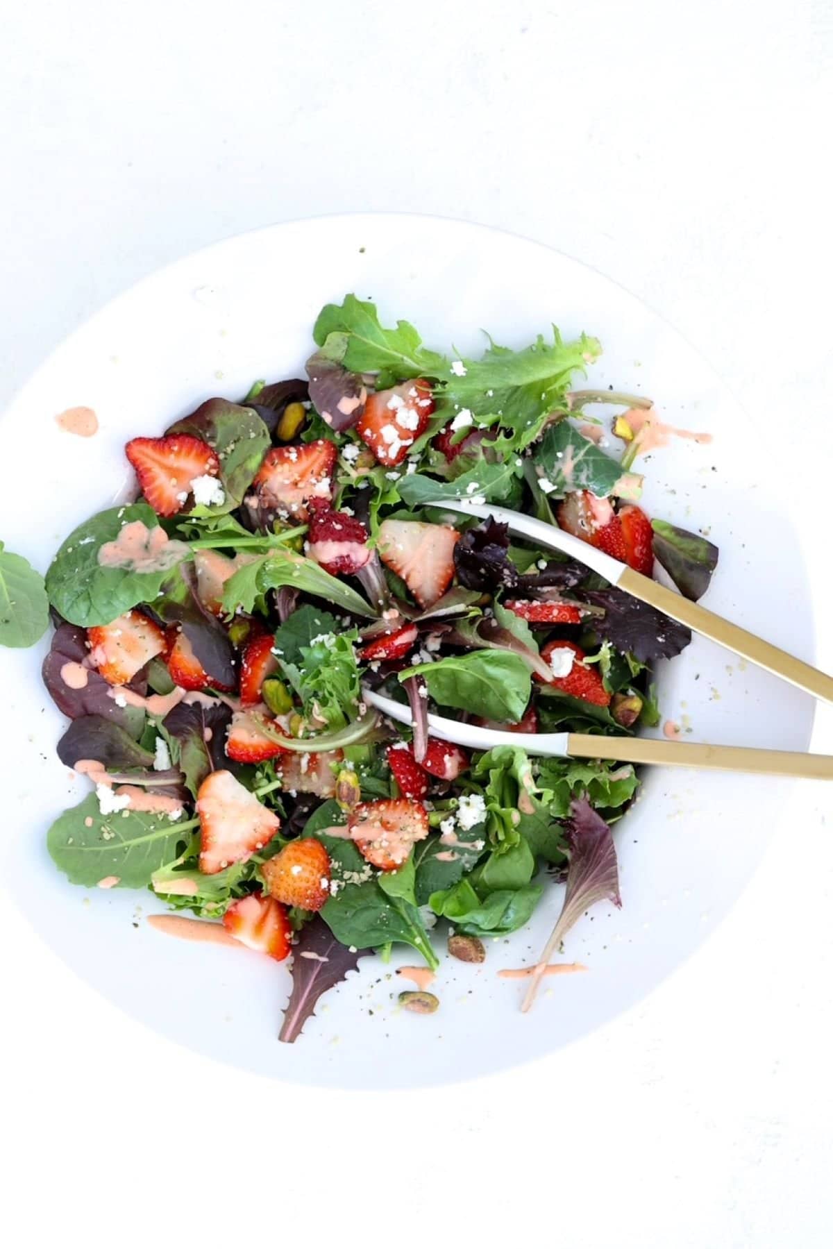 Strawberry Goat Cheese Salad in a large white salad bowl with a pair of tongs.