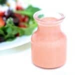 Strawberry balsamic vinaigrette in a glass jar with a salad in the background.