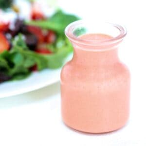 Strawberry balsamic vinaigrette in a glass jar with a salad in the background.