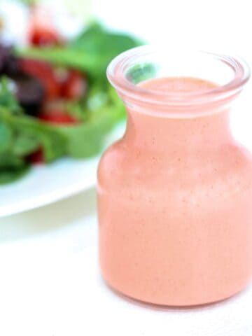 Strawberry balsamic vinaigrette in a glass jar with a salad in the background.