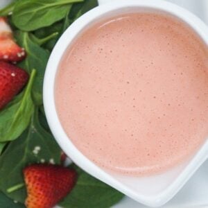 Strawberry salad dressing in a large white creamer cup next to a spinach salad.