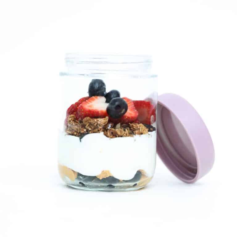 One Greek yogurt parfait with fresh berries in a glass jar with the lid off and leaning on the side of the jar.