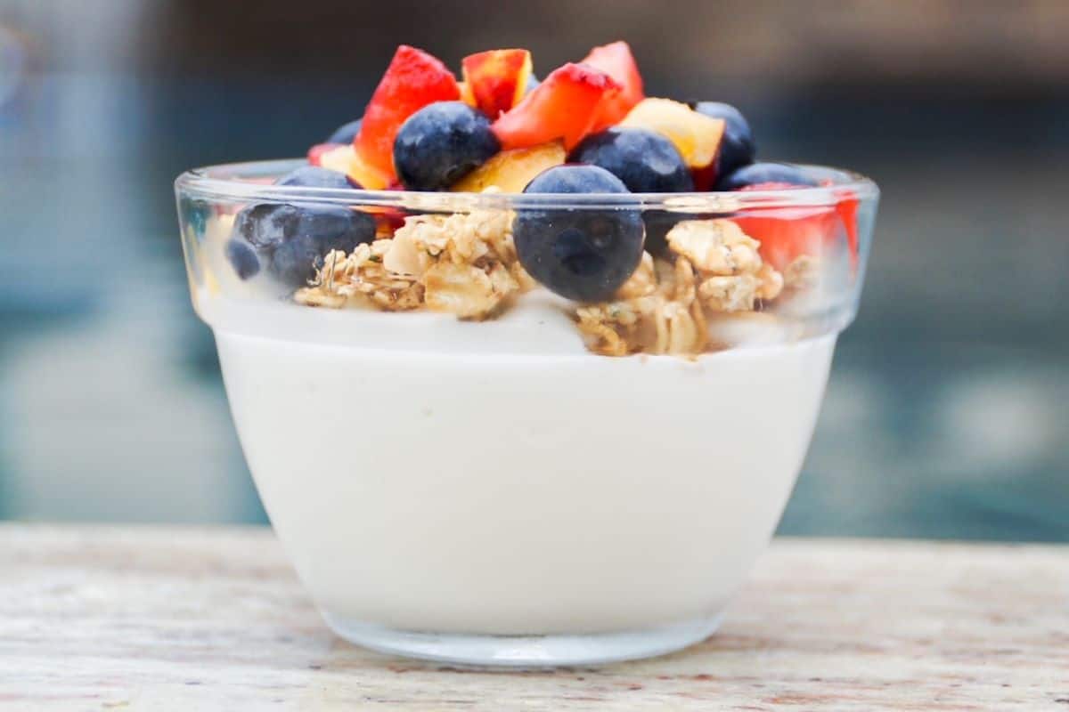 Greek yogurt topped with granola and fresh fruit, served in a small glass dish.