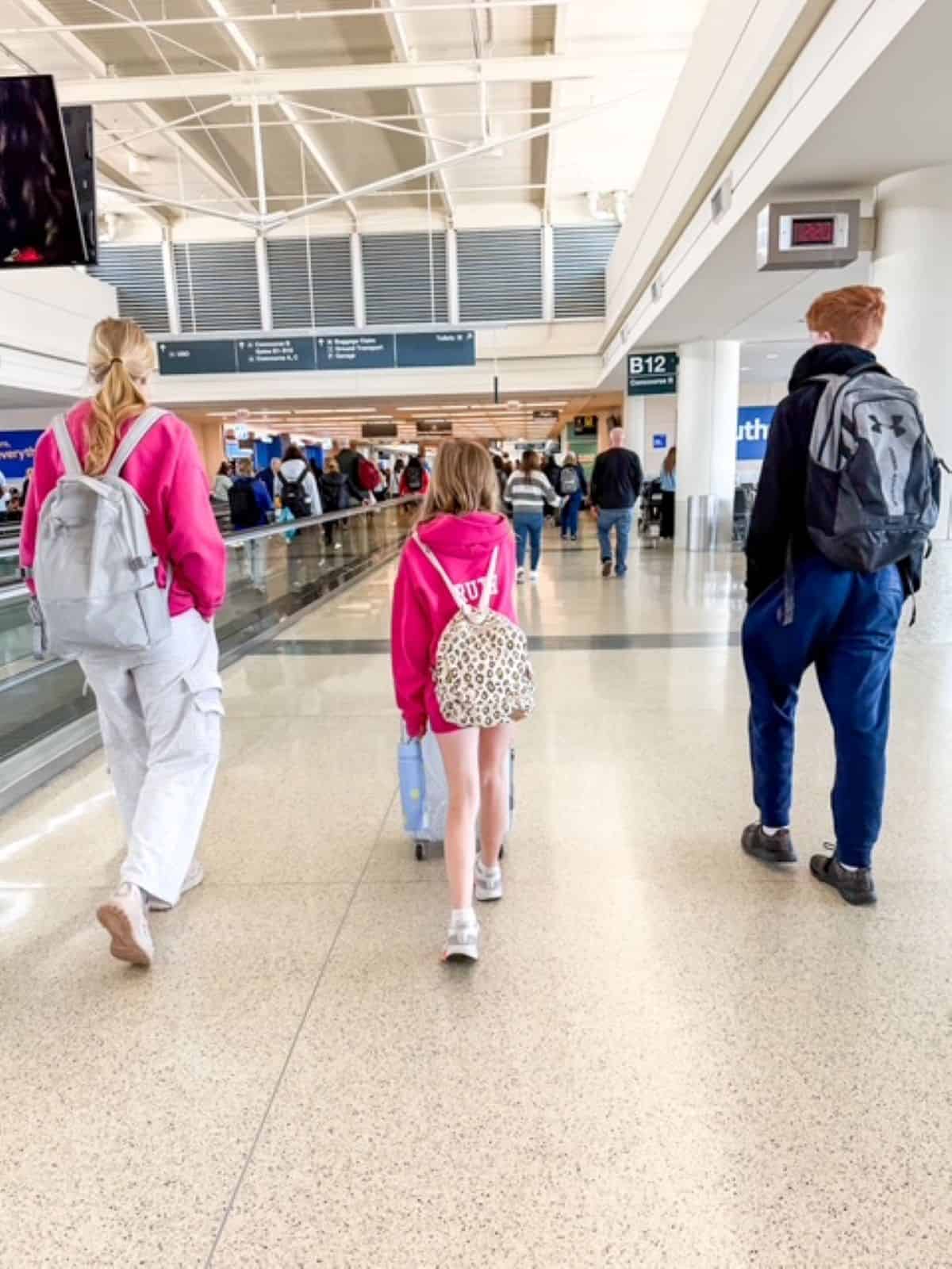 Three kids walking in an airport terminal.