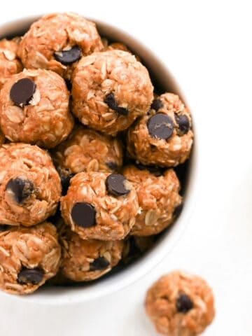 Top view of one white bowl filled with bliss balls. A few bliss balls are to the right of the bowl.