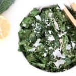 Tuscan Kale Salad with lemon garlic dressing and parmesan in a white bowl with serving tongs.