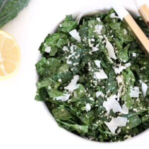 Tuscan Kale Salad with lemon garlic dressing and parmesan in a white bowl with serving tongs.