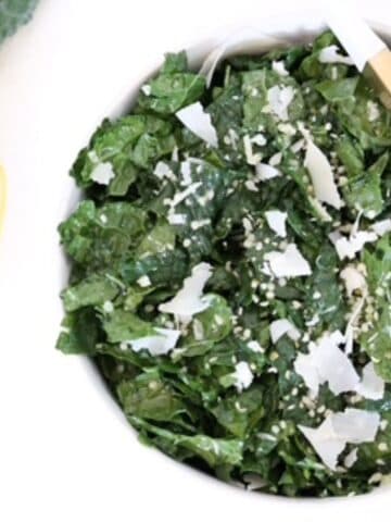 Tuscan Kale Salad with lemon garlic dressing and parmesan in a white bowl with serving tongs.
