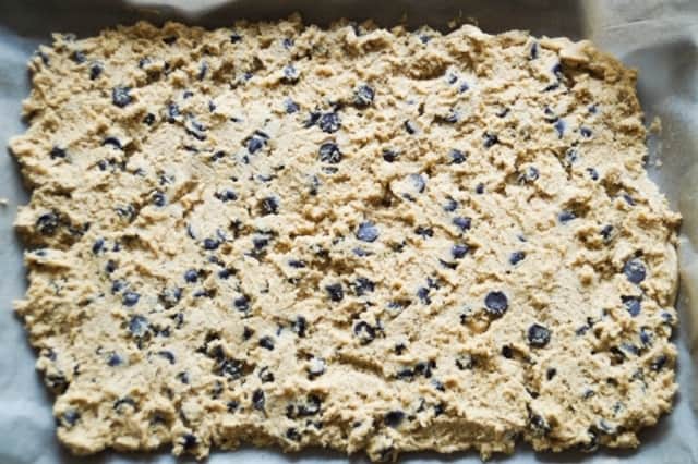 chocolate chip cookie dough spread out on parchment paper in a rimmed baking sheet