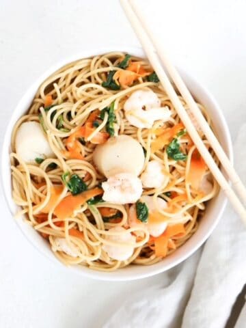 One Asian-inspired noodle bowl with a linen napkin to on the side and chopsticks on the top of the bowl.