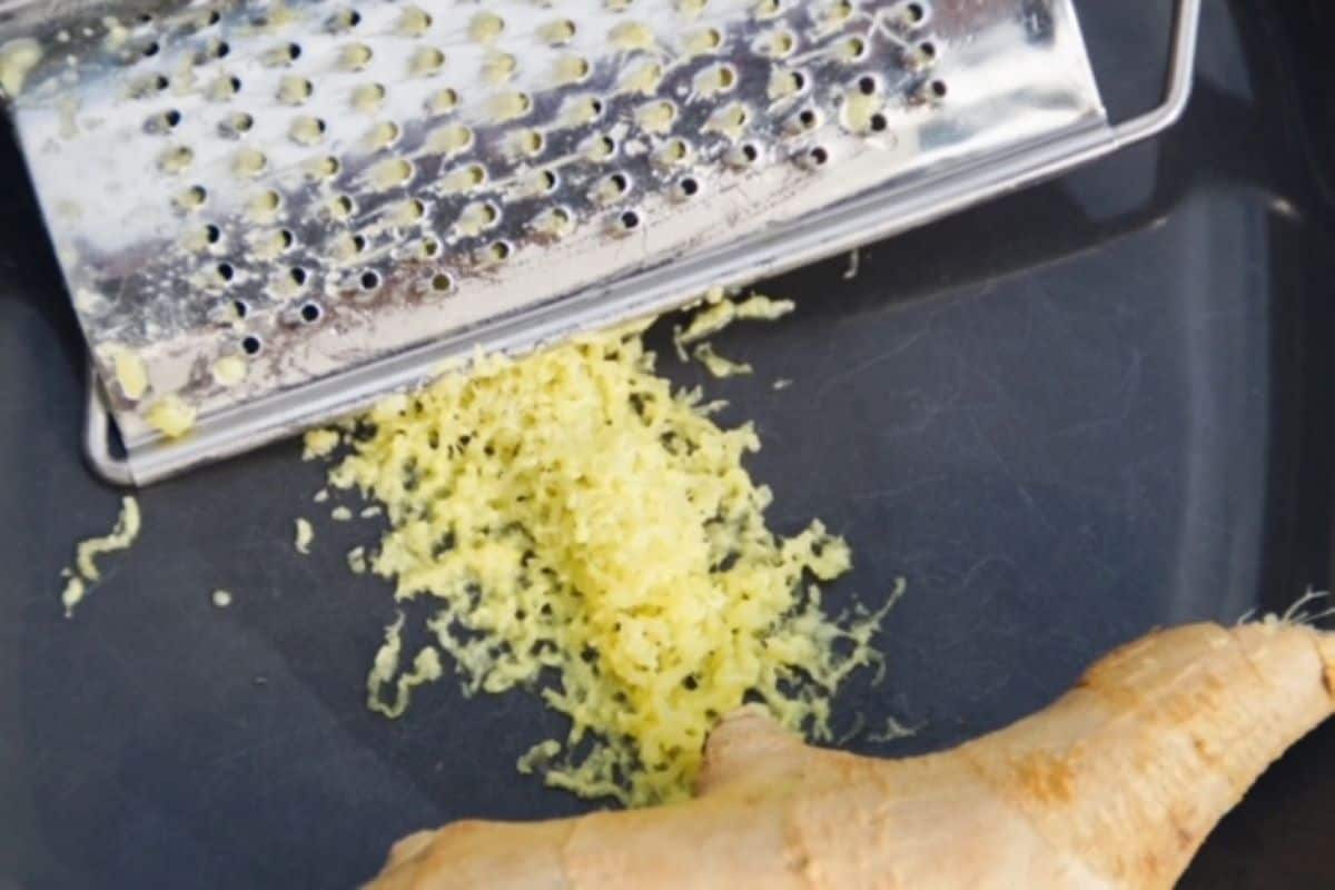 Freshly grated ginger in between a hand-held grater and piece of ginger.