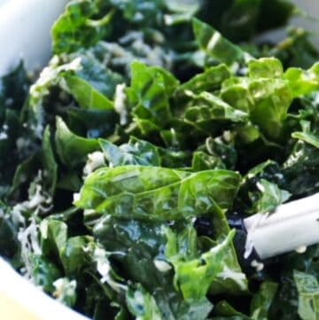 kale salad in a yellow bowl with tongs
