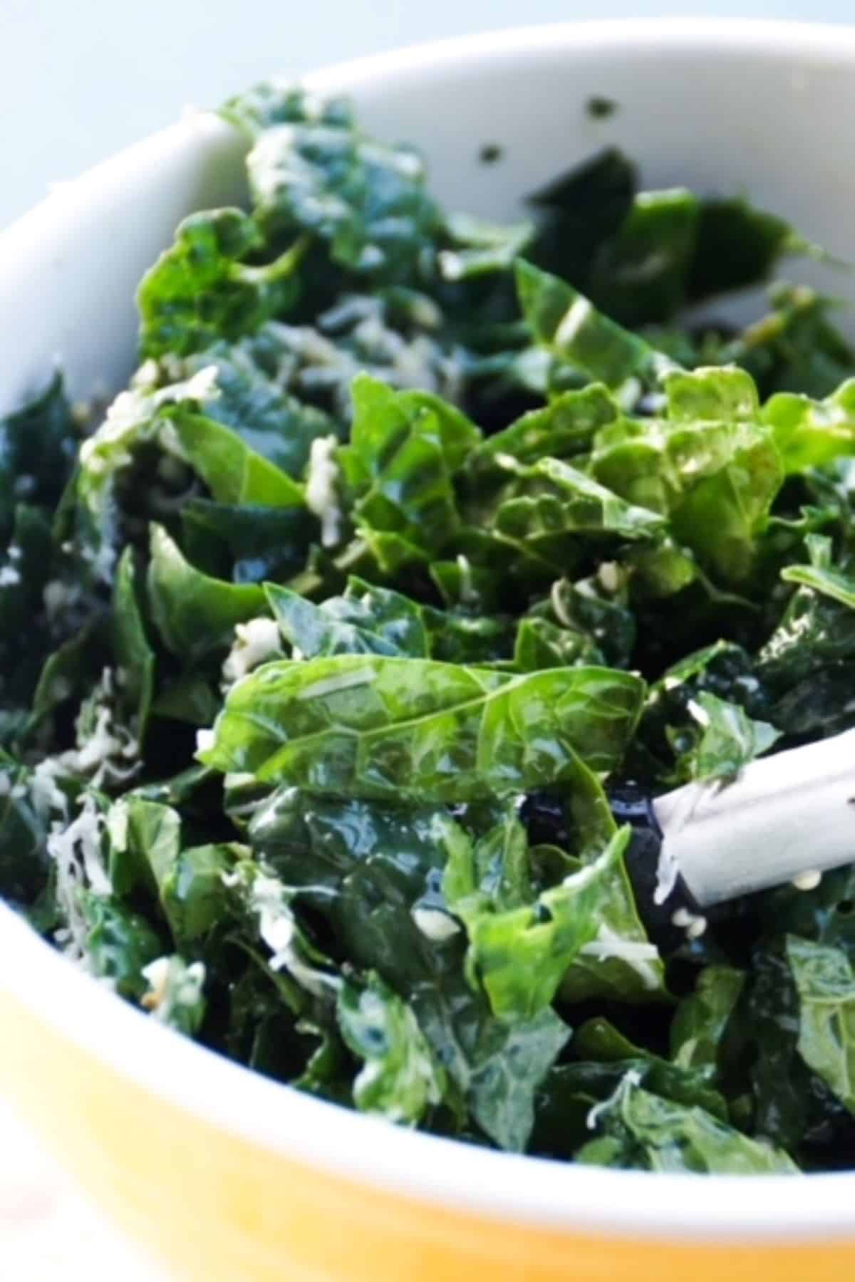 Kale salad in a yellow bowl with tongs.