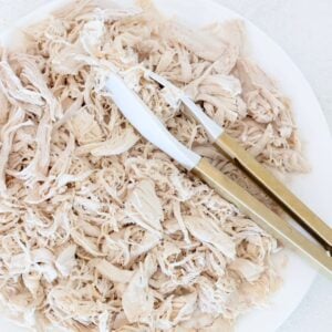 Shredded chicken on a white plate with white and gold tongs.