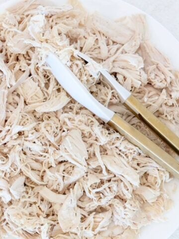 Shredded chicken on a white plate with white and gold tongs.