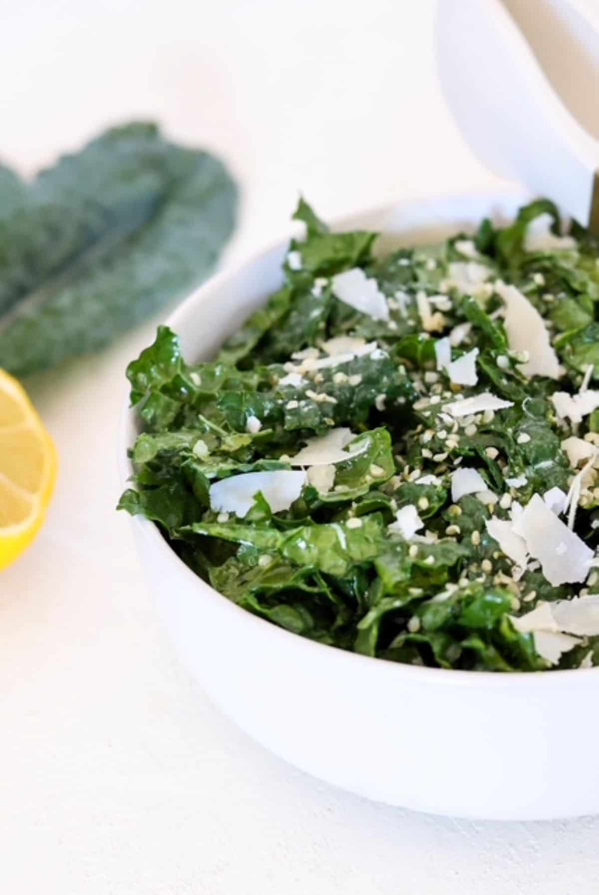 Tuscan Kale Salad in a white bowl with kale and lemon in the background.