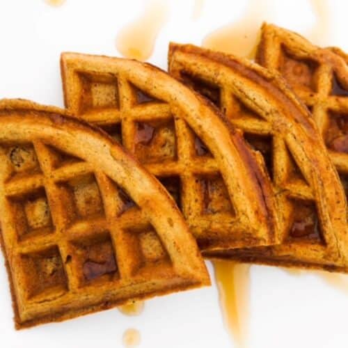 Four pumpkin waffle pieces overlapping on a white plate.