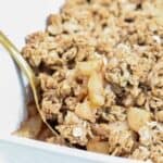 Apple and pear crumble in a white baking dish with a gold spoon.