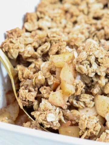 Apple and pear crumble in a white baking dish with a gold spoon.