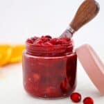 Homemade low sugar cranberry sauce in a glass jar, with the lid and a few cranberries to the side.