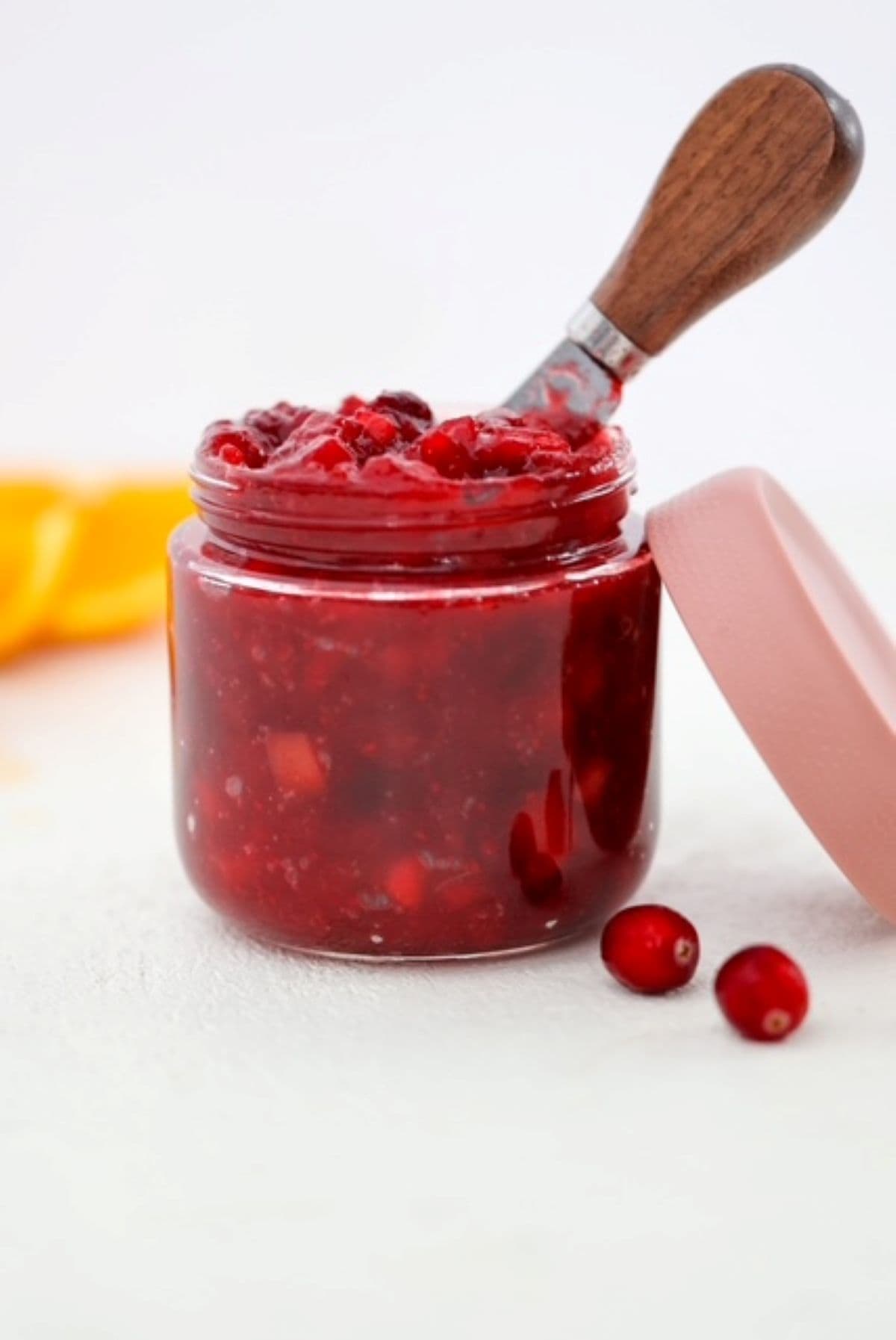 Cranberry sauce in a glass jar with the lid and a few cranberries the side.