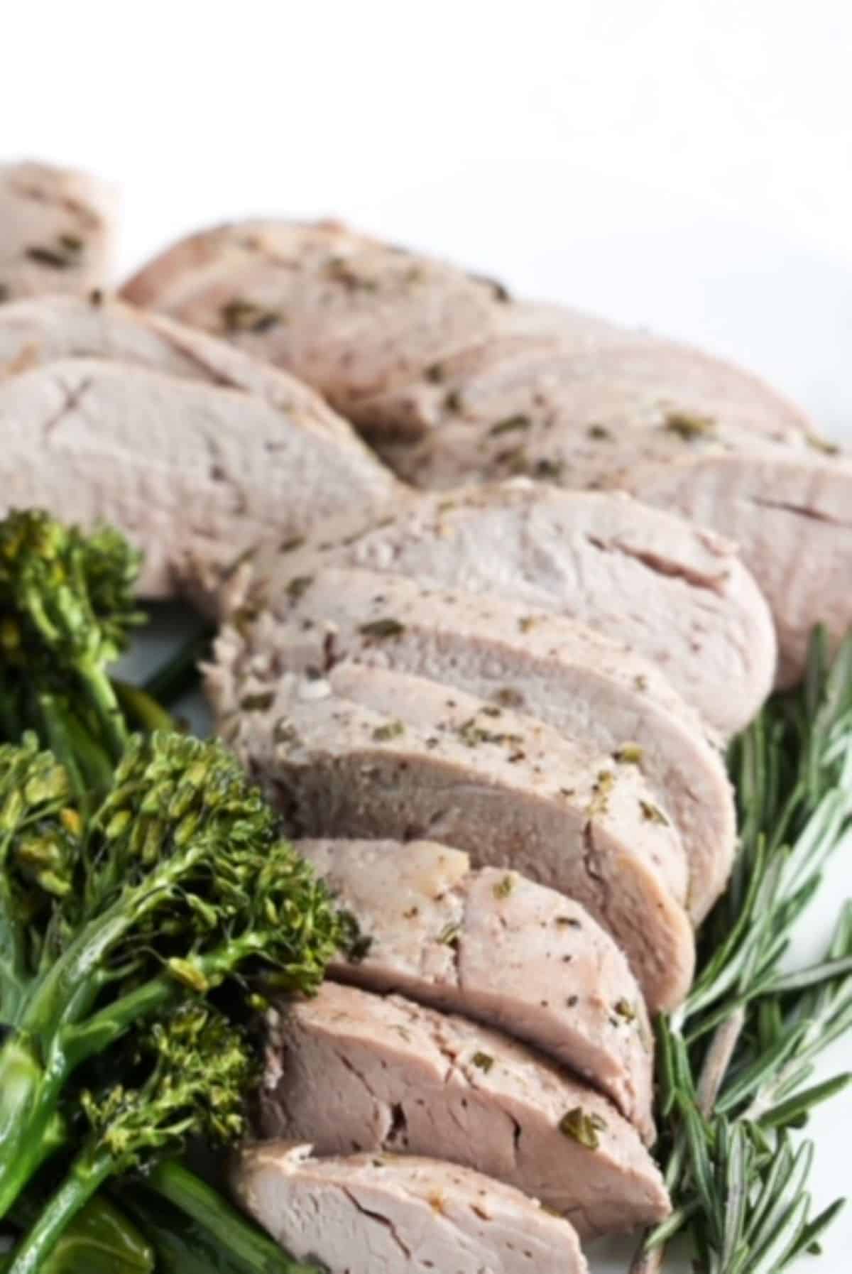 Sliced pork tenderloin with broccolini to the left and a sprig of fresh rosemary to the right.