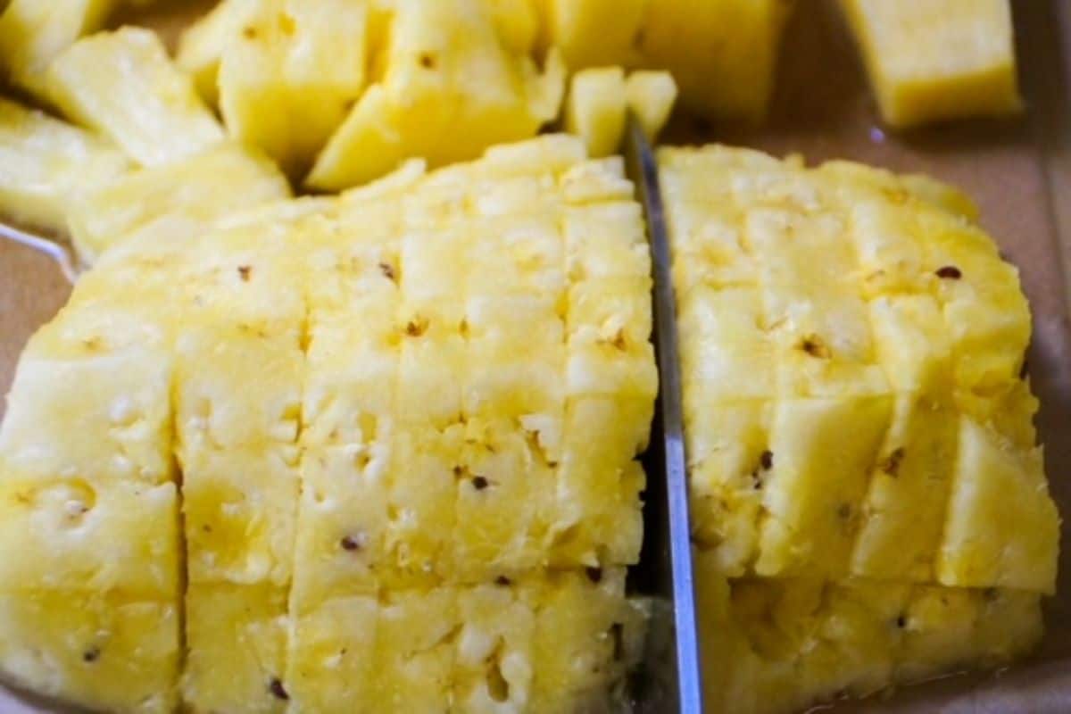 Pineapple being sliced into pieces with a knife.