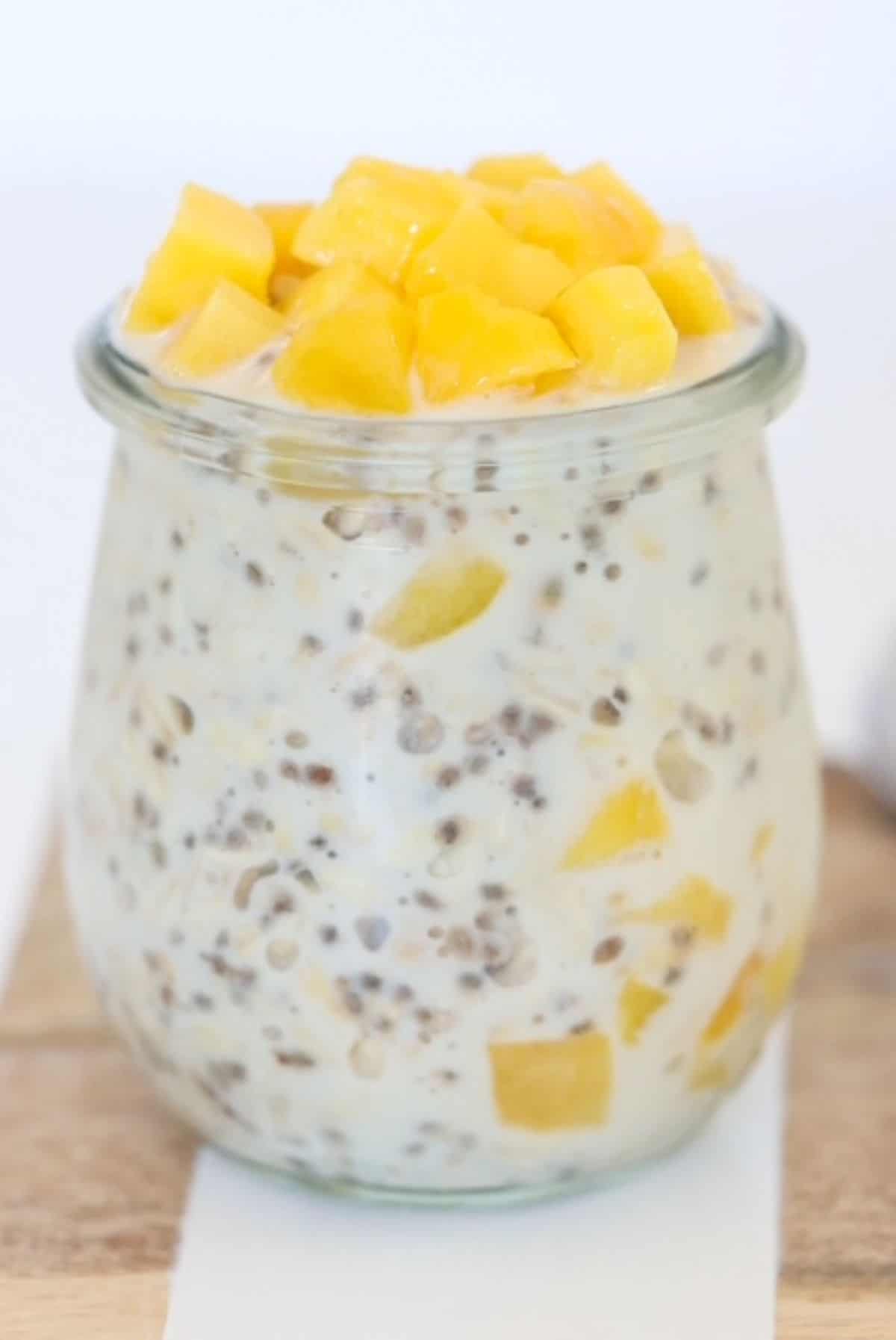 Creamy mango overnight oats in a glass jar topped with chunks of mango.