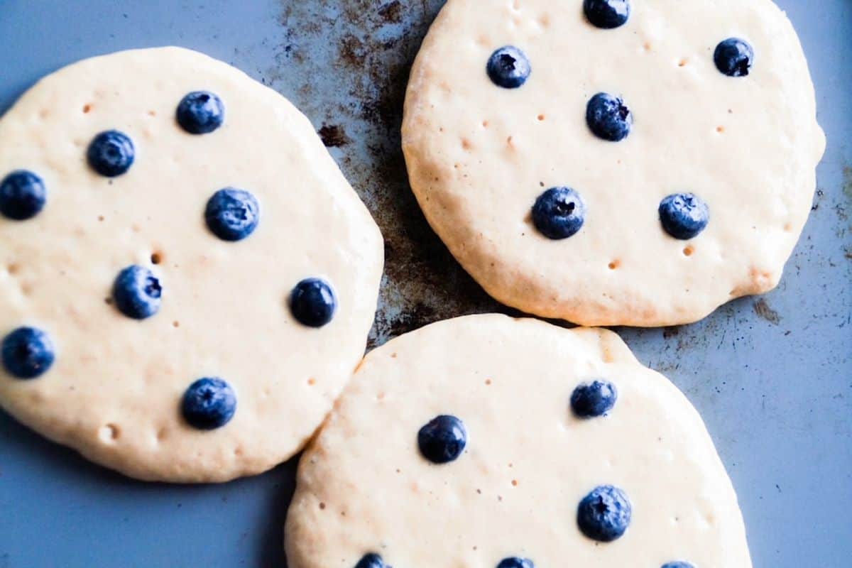 Three blueberry pancakes cooking on a skillet.