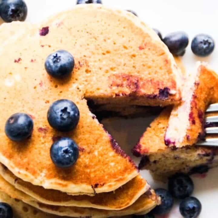 A stack of blueberry pancakes cut into with a fork.